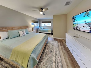 Quarto com cama, televisão, ventoinha no teto e janela.