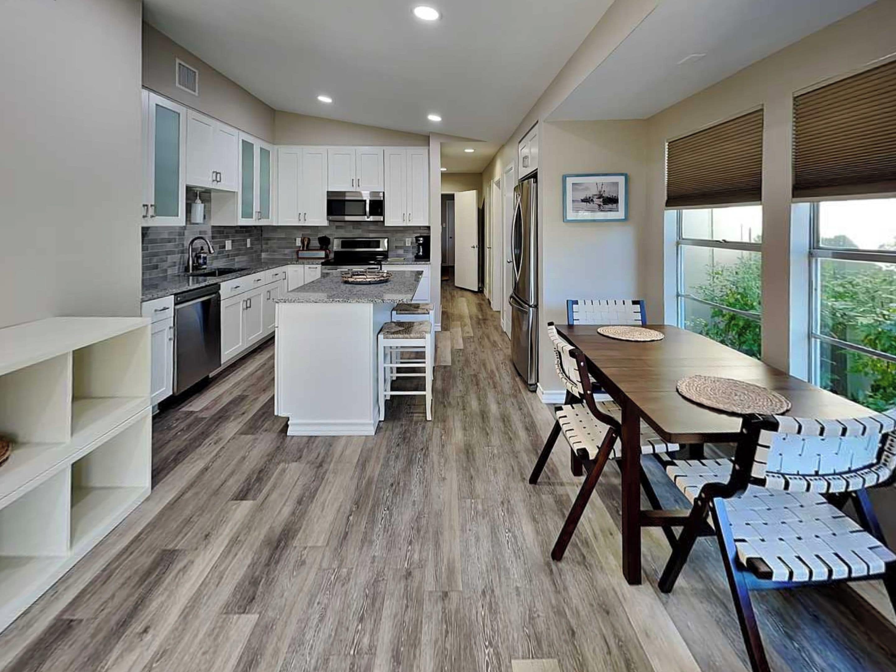 Una cocina moderna con armarios blancos, una isla central y un comedor con mesa y sillas de madera.