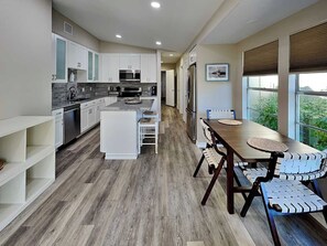 Una cocina moderna con armarios blancos, una isla central y un comedor con mesa y sillas de madera.