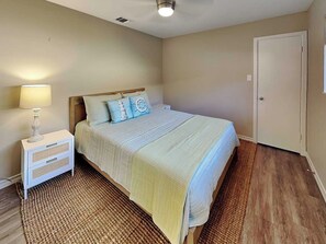 A bedroom with a bed, bedside table, lamp, and a door.