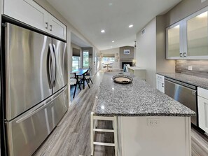 Uma cozinha moderna com eletrodomésticos de aço inoxidável, bancada de granito e área de refeições com mesa e cadeiras.