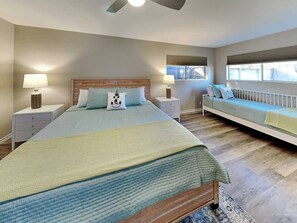 Un dormitorio con una cama grande, mesitas de noche, un banco y un ventilador de techo.