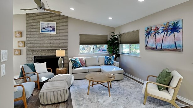A living room with a fireplace, a sofa, a coffee table, and a painting of palm trees. - Little Bay House by Miss Kitty’s (Rockport)