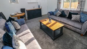 A living room with a sofa, coffee table, and a dining area with a table and chairs. - The Old Well Bungalow - Ty Mawr Farm (Cardiff)