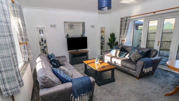 A living room with two grey sofas, a wooden coffee table, a TV, and a blue hanging light fixture. - The Old Well Bungalow - Ty Mawr Farm (Cardiff)