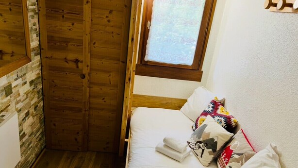 A small, cozy room with a wooden door, a window with a curtain, and a bed with multiple pillows. - A lovely flat right in the centre of Chamonix (Chamonix-Mont-Blanc)
