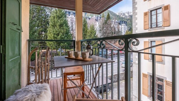A balcony with a table and chairs, a fur-covered bench, and a view of buildings and trees. - A lovely flat right in the centre of Chamonix (Chamonix-Mont-Blanc)