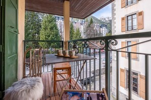 Un balcón con una mesa y sillas, un banco cubierto de piel y vistas a edificios y árboles.
