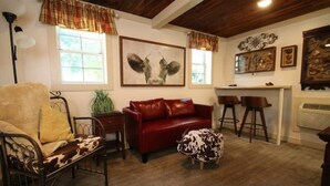 Un salon chaleureux avec un canapé en cuir rouge, une chaise à structure métallique, un pouf à motifs de peau de vache et un grand tableau abstrait accroché au mur.