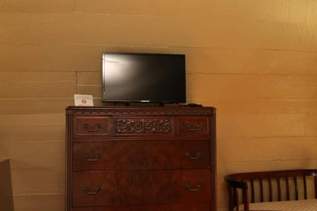 Ein Holzkapfenstück mit einem Flachbildfernseher darauf, ein Sessel und eine Wand mit Backsteinmuster.