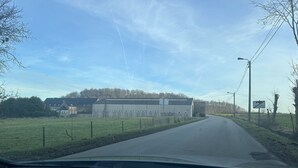 Una strada rurale con un grande edificio industriale sul lato sinistro.