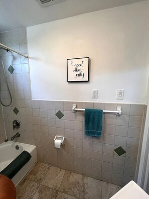Un baño con bañera, un perchero con una toalla azul, un dispensador de papel higiénico y un letrero en la pared que dice 'good vibes only'.