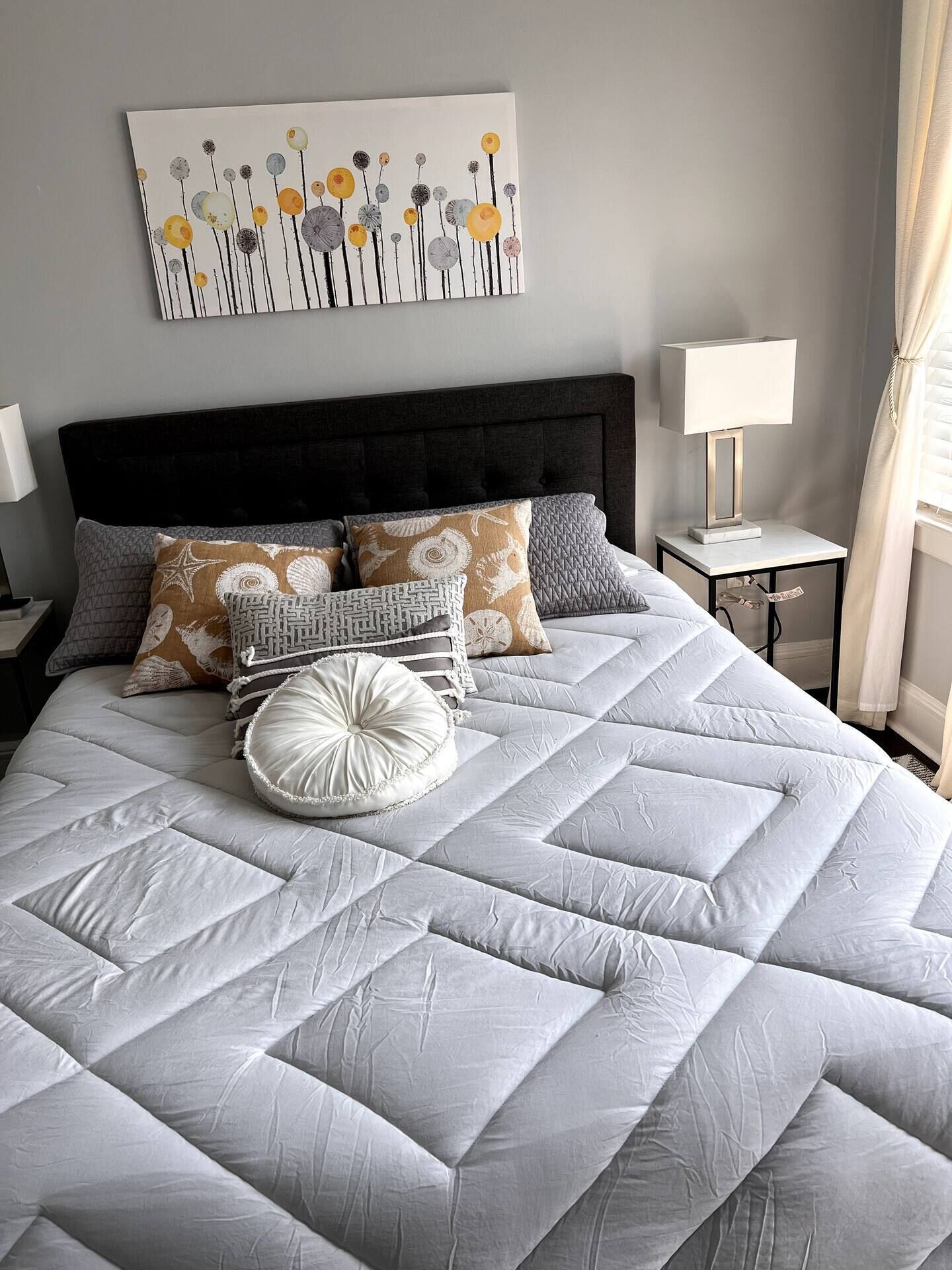 Un lit bien fait, avec une couette matelassée grise, plusieurs oreillers et un coussin décoratif à motifs blancs et gris.