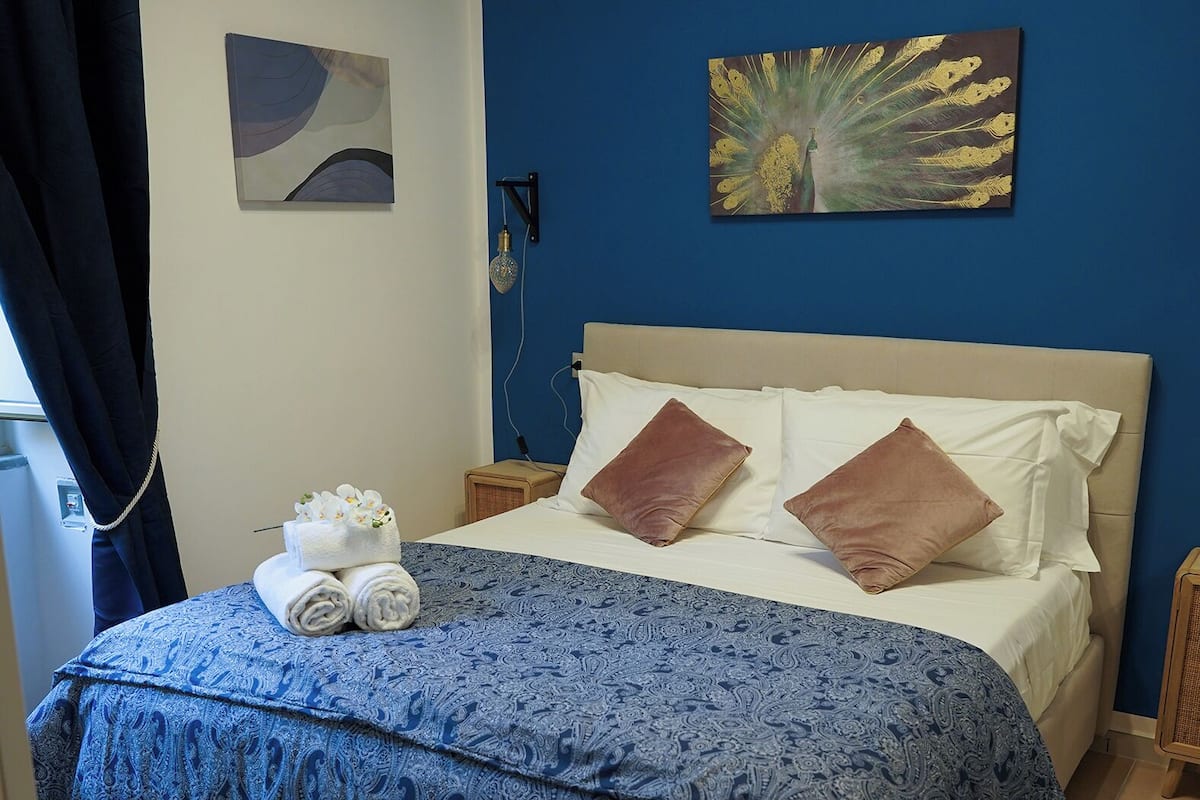 A neatly made bed with a blue patterned bedspread, two pillows, and a set of towels on the side.