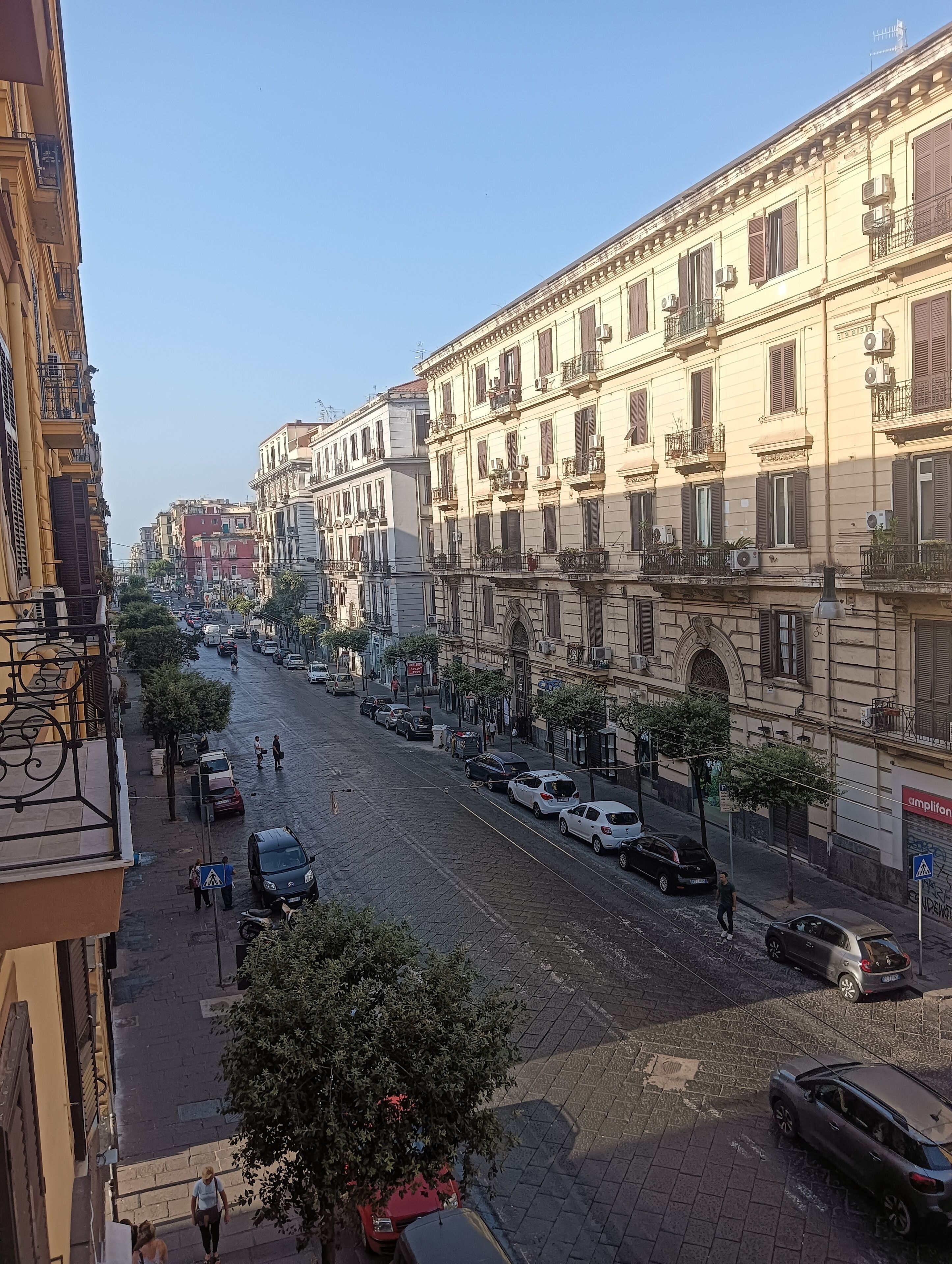 A street view with buildings, parked cars, and pedestrians.