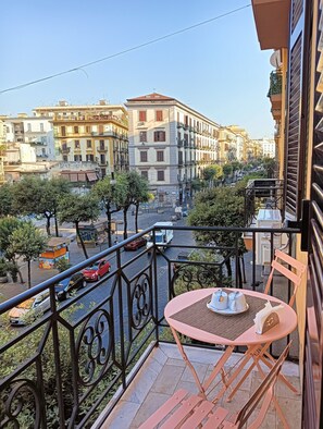 Ein Balkon mit Tisch und Stühlen mit Blick auf eine Straße, gesäumt von Gebäuden und Bäumen.