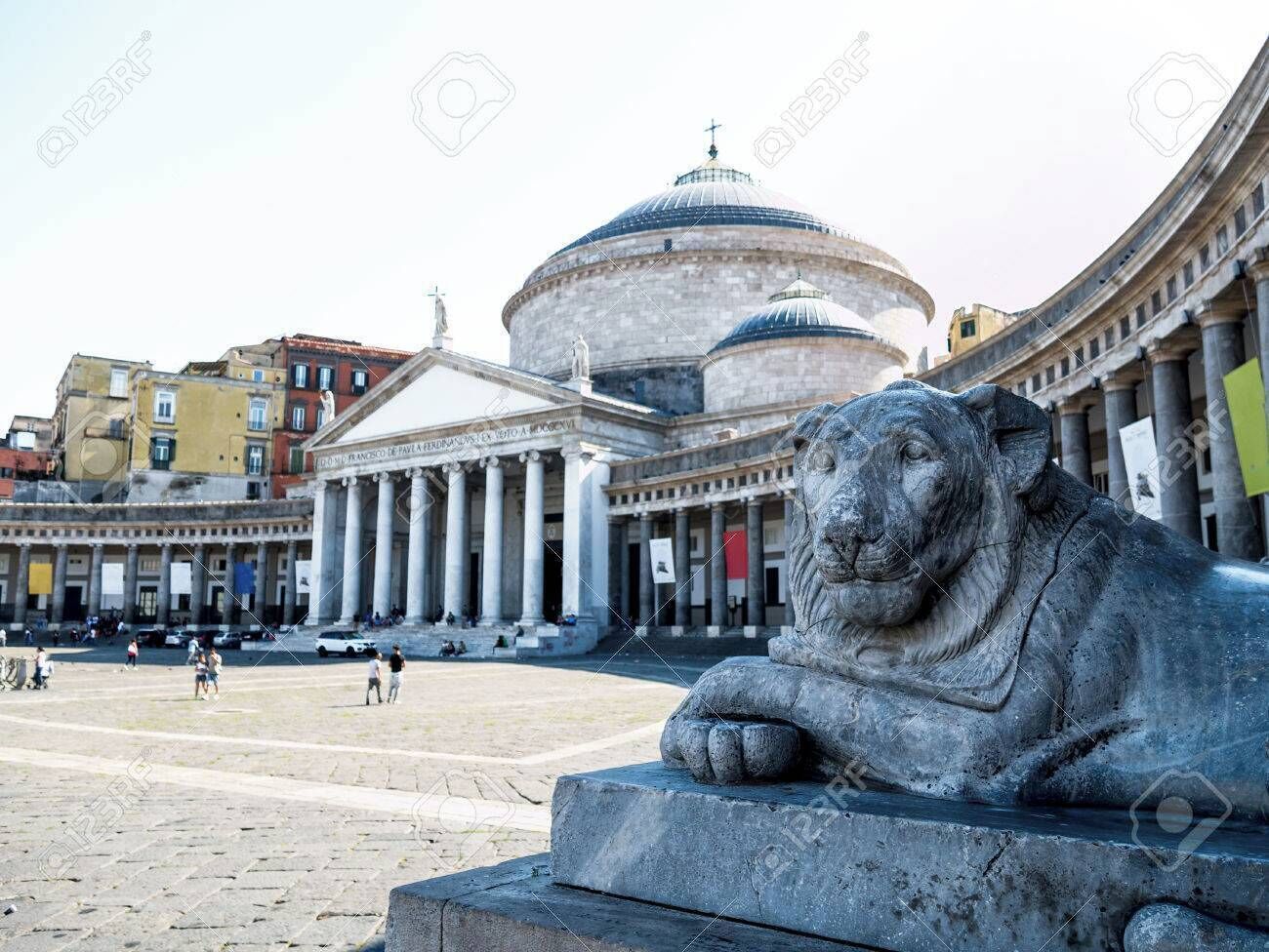 A stone lion statue in a public square with classical architecture in the background.