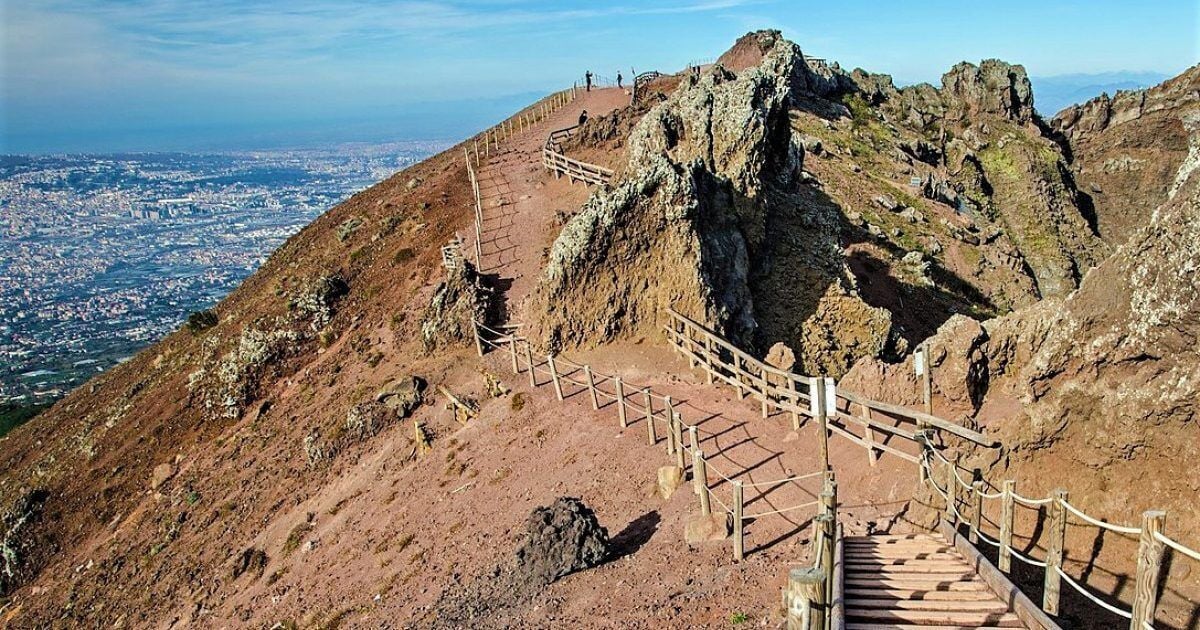 A mountain trail with wooden steps and railings, leading to a rocky peak.