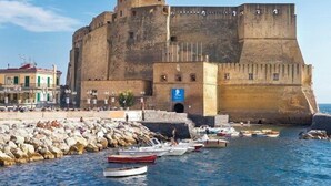 Una fortaleza de piedra histórica con un foso, barcos y un paseo marítimo.