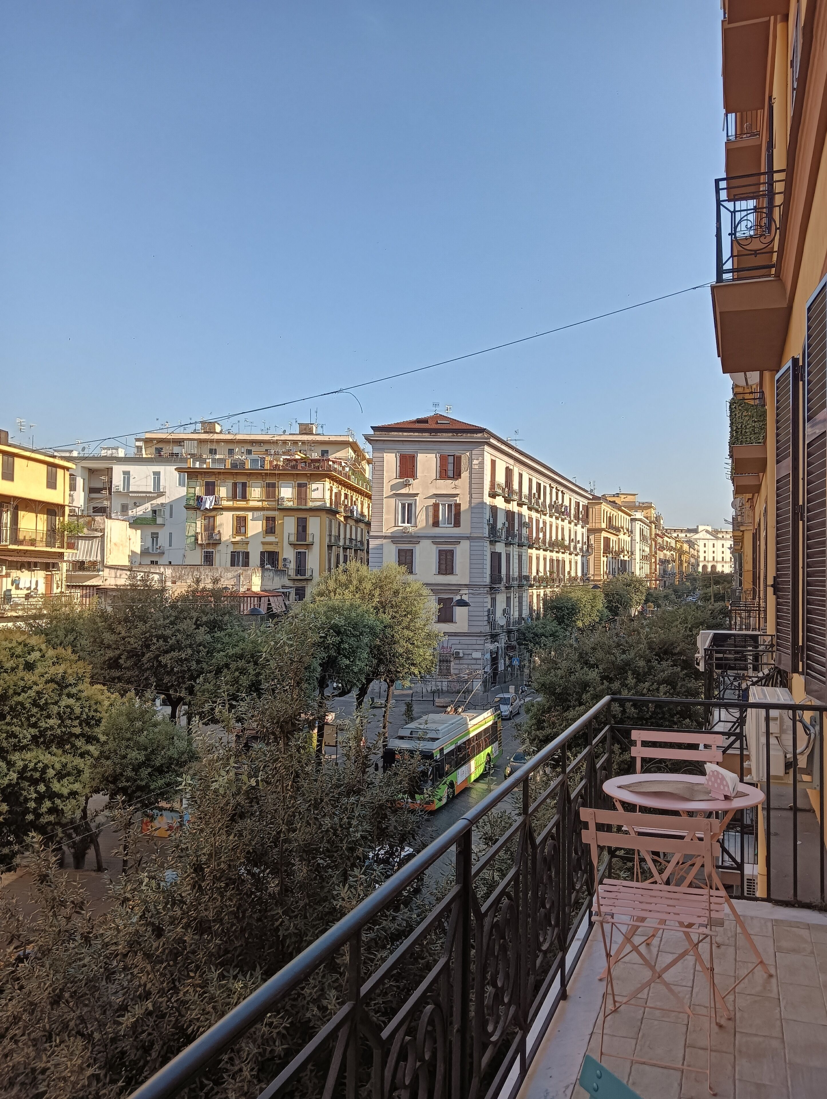 A balcony with a view of a cityscape, featuring multi-story buildings and a street with a bus.