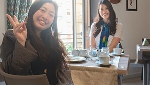 Dos personas sentadas a una mesa con vista a la ventana, un reloj y cuadros en la pared.
