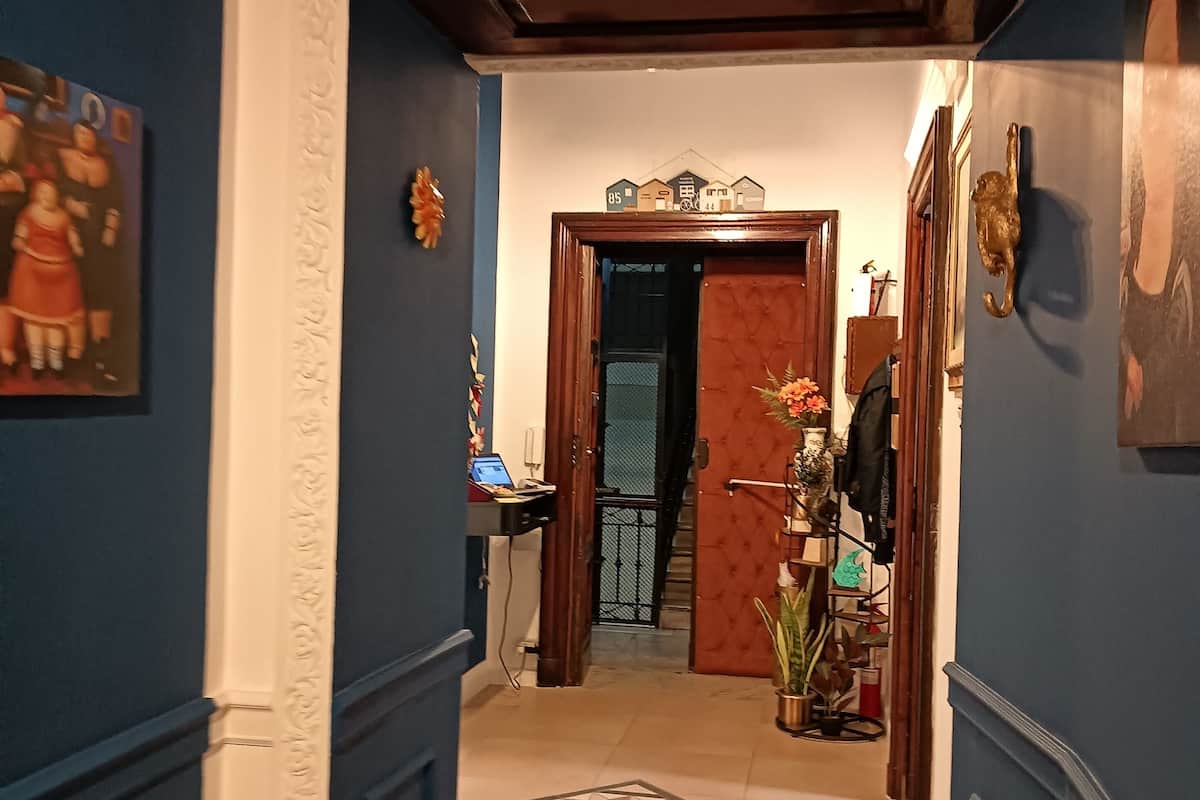 A hallway with blue walls, a patterned floor, and a door leading to a room with a bed.