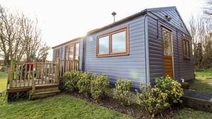 A small, single-story house with a wooden deck and a fenced garden area. - Y Caban Glas (Llandysul)