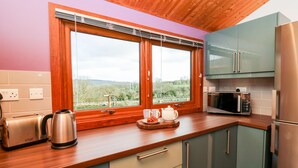A modern kitchen with wooden cabinets, a stainless steel refrigerator, a microwave, and a toaster. - Y Caban Glas (Llandysul)