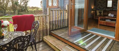 A wooden deck with a glass door leading to a room with a sofa and a table.