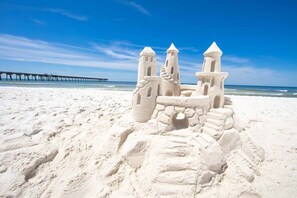 Un château de sable doté de plusieurs tours et entouré d ’un fossé, sur une plage de sable, avec une jetée en arrière-plan.