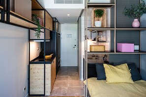 A compact, modern room with built-in shelving, a bed with a yellow bedspread, and a small kitchenette area. - Micampus Porto Asprela (Porto)