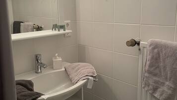 Een kleine badkamer met een wastafel, spiegel, handdoekhouder en een prullenbak.