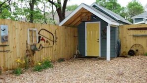 Een klein houten tuinhuisje met een gele deur, een raam en een metalen poort.