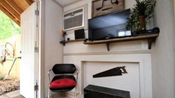 Een kamer met een televisie op een plank, een stoel met een rode kussen en een open haard.