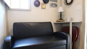 Een woonkamer met een zwarte leren bank, een bijzettafeltje met een lamp en een rode fauteuil.