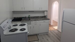 A compact kitchen with white cabinets, a stove, a sink, and a refrigerator. - Nestled in the heart of Pierre, shopping & dining near. (Pierre)