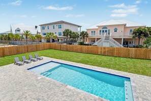 A swimming pool with lounge chairs, a wooden fence, and a two-story house with a balcony. - 4 Bedroom, 2 Bath, Large Heated Pool and Pet Friendly! (Pensacola Beach)