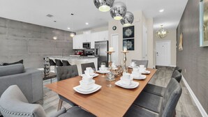 Un comedor moderno con una mesa de madera preparada para cuatro personas, rodeada de sillas tapizadas en gris.