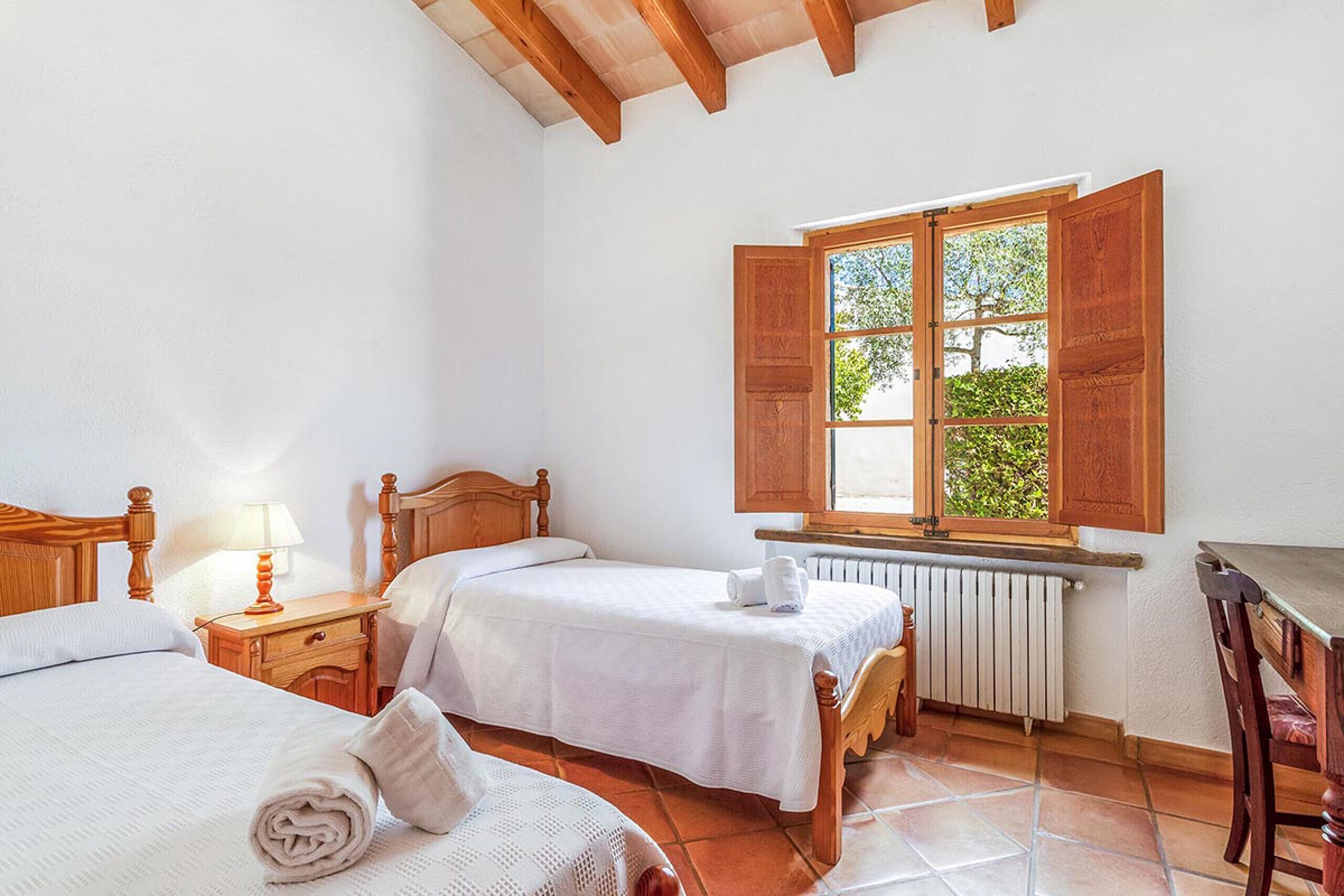Une chambre avec deux lits, une table en bois, une fenêtre avec des volets ouverts et un radiateur.