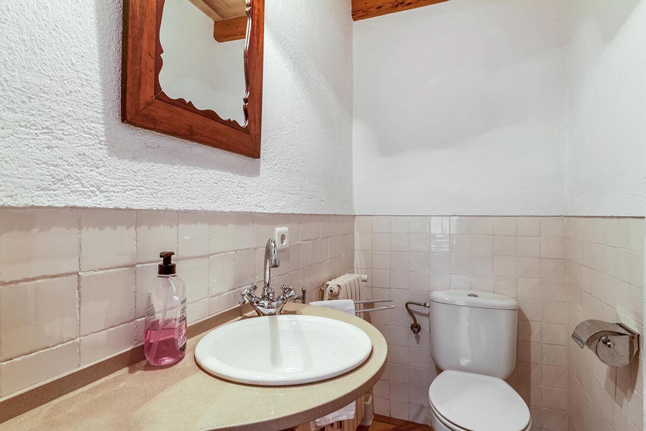 A bathroom with a white sink, a mirror, a toilet, and a soap dispenser.