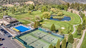 Una cancha de tenis rodeada por un campo de golf, con un edificio al lado de la cancha.