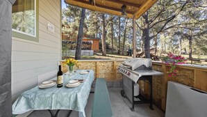 Un patio al aire libre con mesa lista para comer, una parrilla y vistas del bosque circundante.