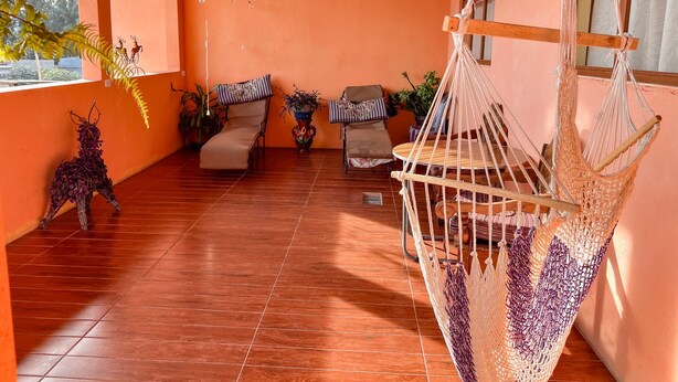 A sunlit patio with a hammock, cushioned chairs, and potted plants. - Cozy Apartment for 2 w/roof. View to Volcanoes (Panajachel)