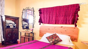 A bedroom with a wooden headboard, a bed with a pink bedspread and floral pillow, a wooden nightstand, a mirror, and a red curtain. - Cozy Apartment for 2 w/roof. View to Volcanoes (Panajachel)