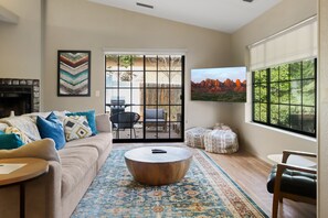 Uma sala de estar com sofá, mesa de centro e vista para o exterior por uma porta de correr.