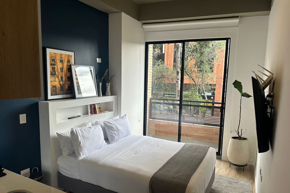 Une chambre à coucher moderne, avec un lit, une table de chevet, une grande fenêtre et une vue sur l’extérieur.
