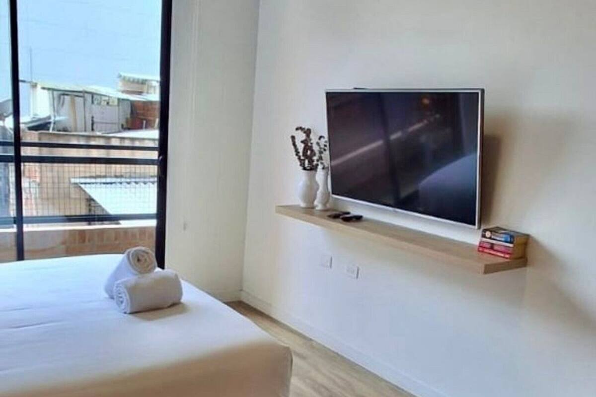 Une chambre moderne avec un lit, un téléviseur posé sur une étagère et une fenêtre donnant sur un beau paysage.
