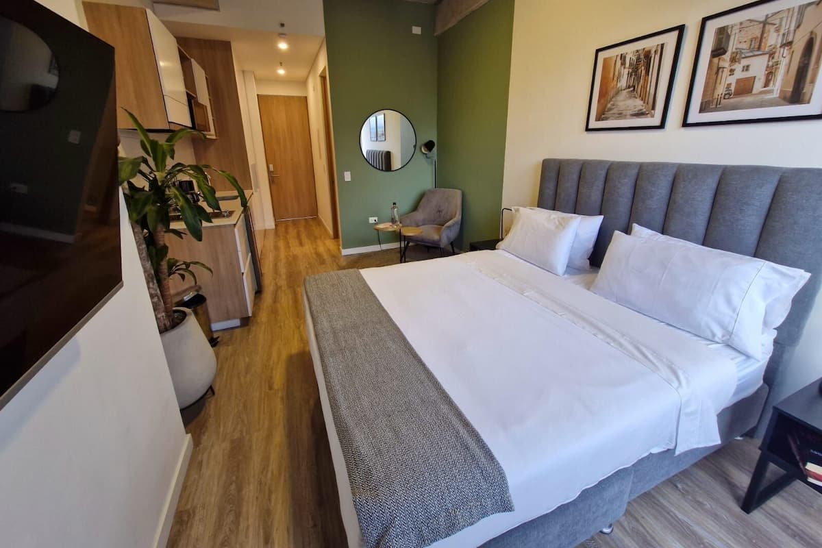 Une chambre d’hôtel avec un lit, une chaise, un miroir et une plante en pot.