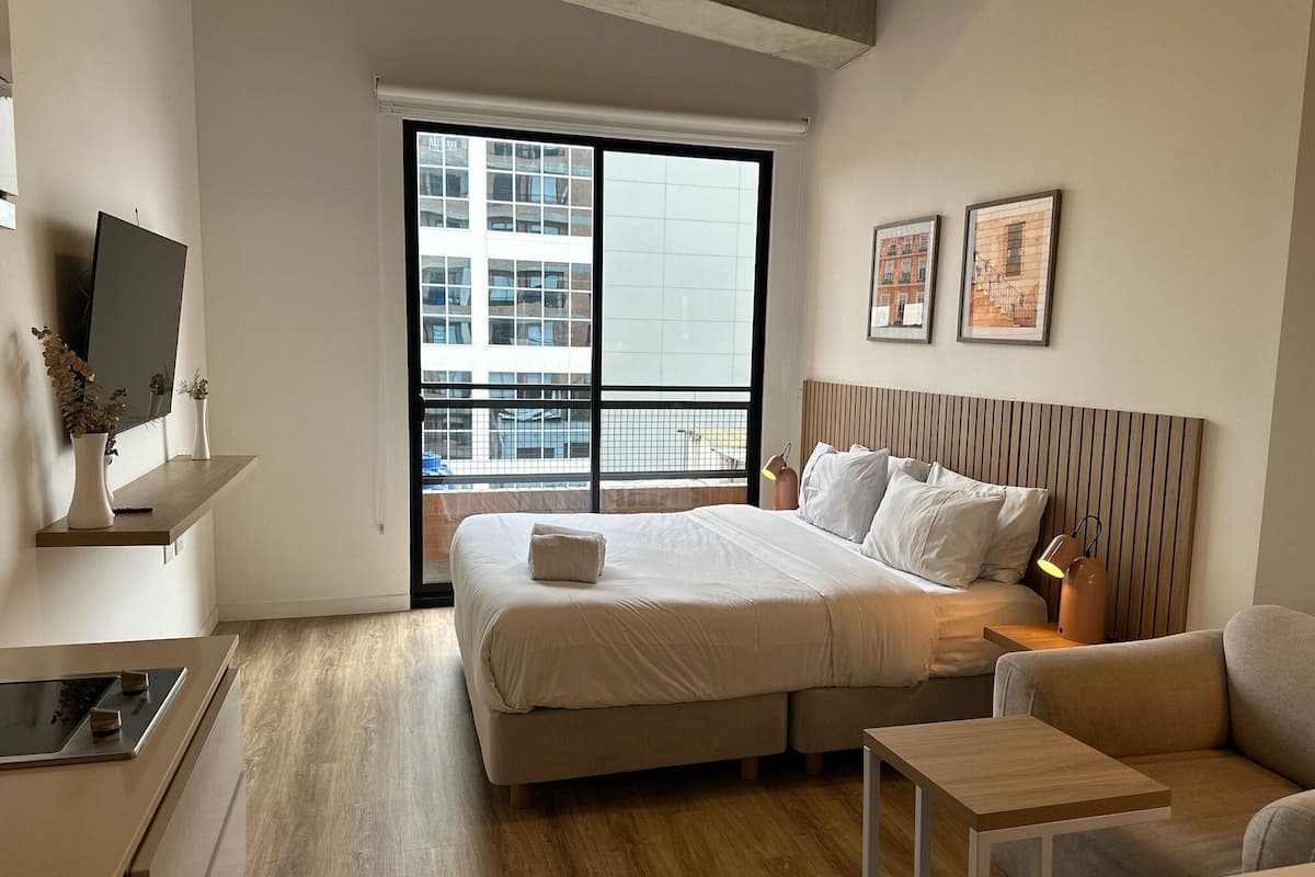 Une chambre d’hôtel moderne équipée d’un lit, d’un canapé, d’une petite table, d’une télévision et d’un balcon offrant une vue sur la ville.