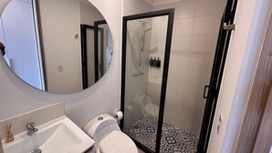 A bathroom with a toilet, sink, mirror, shower, and tiled floor. - U-GO Edificio Next Living Bogota (Bogotá)